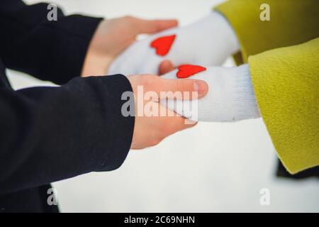 Nahaufnahme Hände von netten Paar in der Winterstraße. Mann halten Hände der Freundin. Kleine rote Herzen auf Handschuhe der Frau. Liebeskonzept. Liebe wärmt Menschen Stockfoto