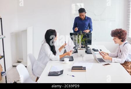 Internationale Gruppe von Frauen diskutieren Business Deal, afrikanische Coach im Büro mit weißen Innenraum Stockfoto