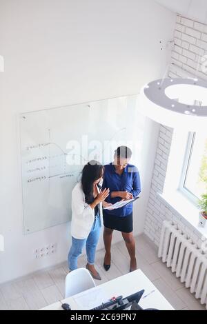 Draufsicht auf die Durchführung von Business-Schulungen. Afrikanische Geschäftsfrau stehend mit asiatischen Frau sprechen. Weiß Innenbüro Stockfoto