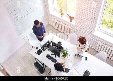 Internationale Partner tauschen Erfahrungen aus der Arbeit im Geschäft aus. Draufsicht auf drei Frau diskutieren, afrikanischen Trainer stehen zu anderen sprechen. Weiß ich Stockfoto