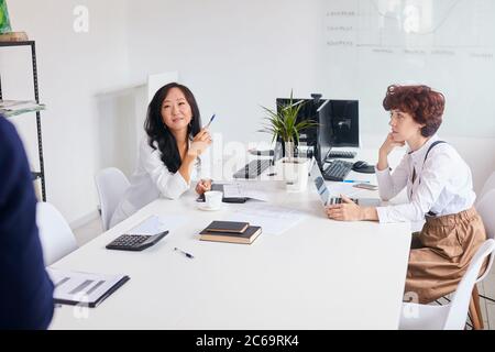 Blick von hinten auf den Trainer, asiatische und kaukasische Frauen sitzen auf dem Tisch hören Sie neue Business-Plan mit Trainer Stockfoto