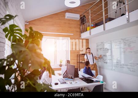 Junge multi-ethnische Team von Geschäftspartnern sitzen hören erfolgreich sprechen von erfahrenen Mann zeigt, wie sein Geschäft Entwicklung in Flipchart. So Stockfoto