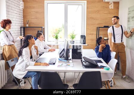 Erfolgreiche Präsentation des jungen kaukasischen Mannes mit Flipchart, isoliert im Büro. Multiethnische Gruppe von Zuhörern Stockfoto