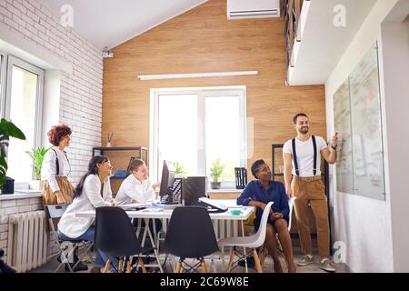 Erfolgreiche Präsentation des jungen kaukasischen Mannes mit Flipchart, isoliert im Büro. Multiethnische Gruppe von Zuhörern Stockfoto