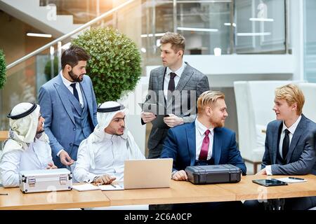 Kaukasische Geschäftsleute in Anzügen zeigen neue Technologie in schwarzem Gehäuse. Internationale Tagung im Business Center Stockfoto