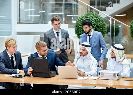 Kaukasische Geschäftsleute in Anzügen zeigen neue Technologie in schwarzem Gehäuse. Internationale Tagung im Business Center Stockfoto