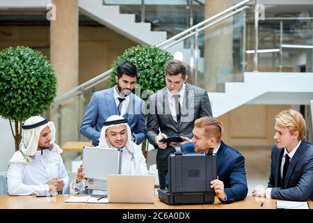 Kaukasische Geschäftsleute in Anzügen zeigen neue Technologie in schwarzem Gehäuse. Internationale Tagung im Business Center Stockfoto