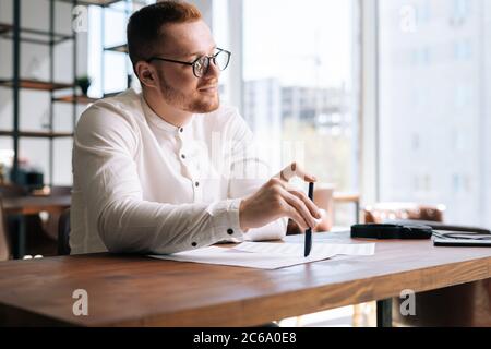 Nachdenklicher junger Mann, der Mode-Freizeitkleidung und stilvolle Brillen trägt, schreibt Text auf Papier Stockfoto