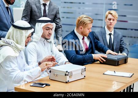 Treffen der kaukasier und araber. Sitzen auf dem Tisch mit den Koffern, kaukasische Männer in den Anzügen, Scheichs in den weißen Anzügen. Amerika und saudi-arabien, dubai Stockfoto