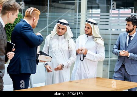 Zwei junge Geschäftsleute aus dubai hören kaukasischen Geschäftsmann zu Stockfoto