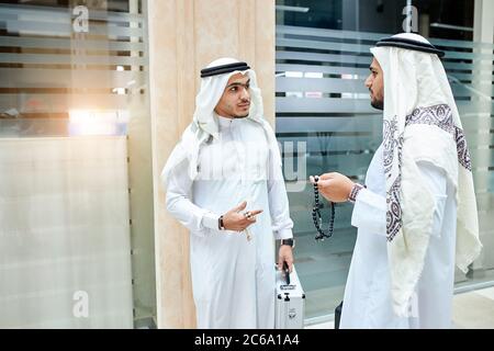 Zwei arabische Männer mit Fällen sprechen, reden. In weißen Anzügen. Business Center, Background Stockfoto