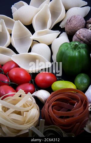 Bunte und bunte Pasta in großer Zahl und in verschiedenen Farben zusammen mit verschiedenen Früchten und Gemüse. Stockfoto
