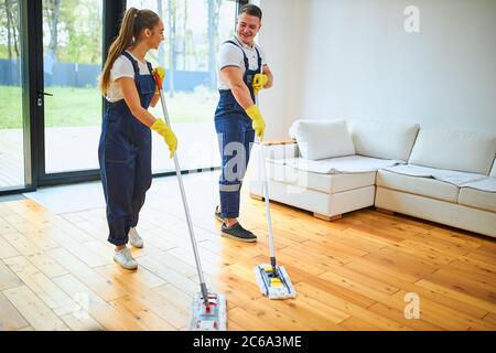 Die Teamarbeit der professionellen Hausmeister in der einheitlichen Arbeit zusammen waschen Holzboden Stockfoto