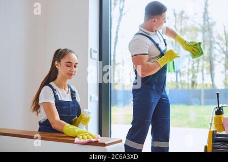 Vorbereitung Wohnung für den Verkauf. Tragen von Uniform, gelben Gummihandschuhen, Sprays. Abwischen von Staub, Reinigen, Waschen von Glas des Fensters Stockfoto