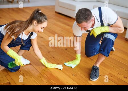Zwei Hausmeister in blauen Uniformen Polieren Holzboden mit Lumpen. Tragen Schutzhandschuhe aus Gummi Stockfoto