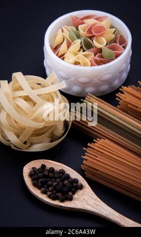Lange braune Pasta und geformte Pasta neben einer Schüssel mit schwarzem Pfeffer. Stockfoto