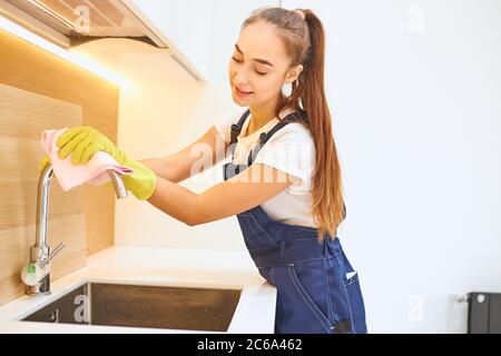 Attraktive Dame Hausmeister effektiv in der Reinigung arbeiten, genießen Sie Arbeit. Frau trägt gelbe Schutzhandschuhe aus Gummi, Arbeitsuniform wischen Stahl s Stockfoto