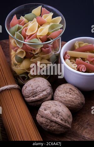 Lange braune Pasta und farbige Pasta in verschiedenen Größen mit ein paar Walnüssen. Stockfoto