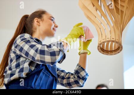 Reinigungsservice, verschiedene Pulver, reinigungsmittel. Mitarbeiter trägt blaue Uniform, in gelbem Gummi-Schutzhandschuh mit trockenem Mikrofasertuch, das Staub abwischt Stockfoto