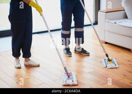 Nahaufnahme der Beine der Hausmeister, die den Holzboden mit Mops waschen. Reinigungskonzept Stockfoto