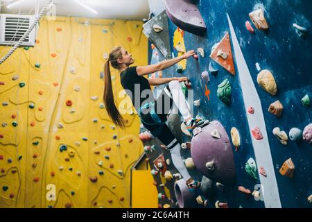 Junge Frau, die eine große, von Männern gemachte Kletterwand klettert Stockfoto