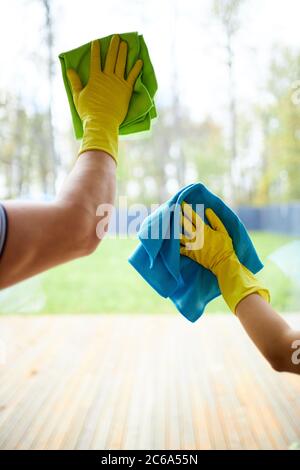 Nahaufnahme von Reinigungsmitteln, die Lumpen halten und gelbe Gummihandschuhe tragen. Reinigen des Fensters Stockfoto