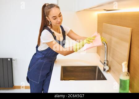 Junge weibliche Arbeiter der Reinigung Service wischen Stahlwaschbecken, Holz-Interieur, modern Stockfoto