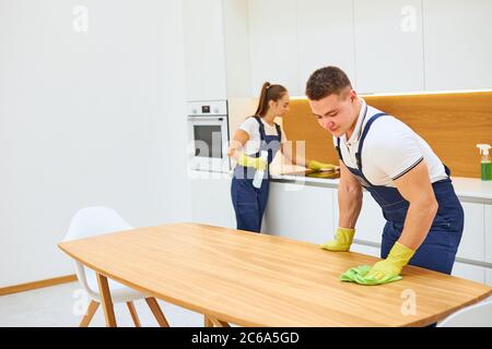 Zwei junge Putzfrauen in Uniform arbeiten effektiv und schnell in der Küche zusammen. Youn kaukasischen Mann wischen Küchentisch, Frau wischen sensorische elektrische Stockfoto