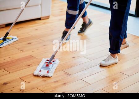 Nahaufnahme der Beine der Hausmeister, die den Holzboden mit Mops waschen. Reinigungskonzept Stockfoto