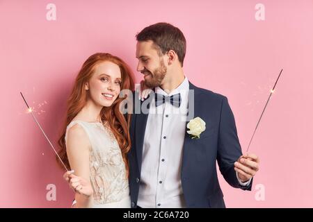 Kaukasisches Paar in Smoking, weißes Hochzeitskleid. Glückliche zwei Menschen halten Wunderkerzen in den Händen. Liebeskonzept Stockfoto