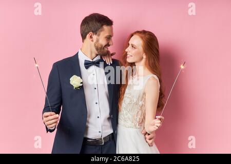 Kaukasisches Paar in Smoking, weißes Hochzeitskleid. Glückliche zwei Menschen halten Wunderkerzen in den Händen. Liebeskonzept Stockfoto