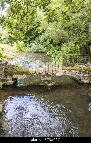 Eine winzige Steinklappenbrücke über den kleinen Fluss Windrush, der durch das Cotswold-Dorf Naunton, Gloucestershire, Großbritannien, fließt Stockfoto