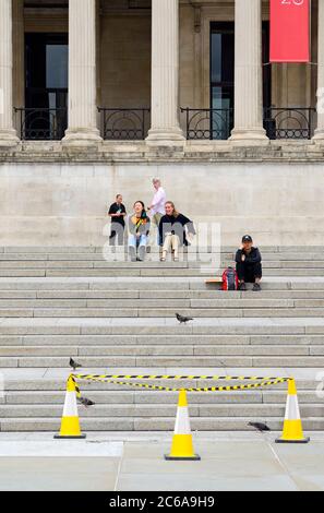 London, England, Großbritannien. Menschen sitzen auf den Stufen zur Nationalgalerie am Trafalgar Square während der COVID-19 Pandemie, Juli 2020 Stockfoto