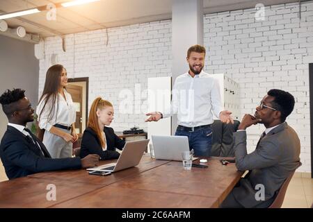 Geschäftsleute halten Konferenzen im Business Center in einem modernen Büro ab. Das internationale Team hört uns, wie uns der kaukasische bärtige Mann in einem weißen Hemd zuhört Stockfoto