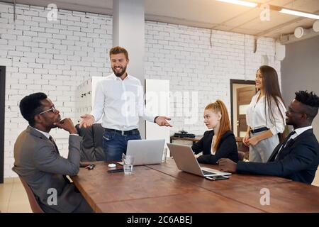 Junge Leute halten Konferenz im Business Center in modernen Büro, um professionelle Geschäftsmann zu hören. Bärtiger Mann trägt weiße formelle Hemd, Stockfoto