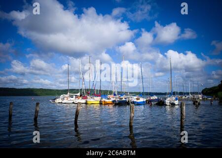 Auf einem See liegen viele Segelboote nebeneinander an einer Landungsstelle und der Himmel ist blau mit weißen Wolken Stockfoto