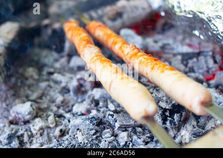 Fleischwürste werden auf heißen Kohlen gebraten. Kochen im Freien. Stockfoto