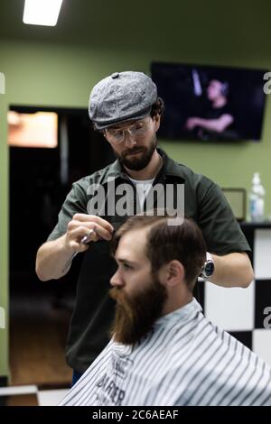 Portrait von attraktiven jungen Mann immer trendy Frisur. Männliche Friseur Dienst Client, machen Haarschnitt mit Metallschere Stockfoto