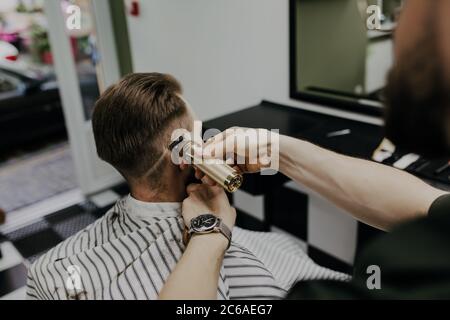 Schöner bärtiger Mann bekommt neue Frisur mit Rasiermesser von Friseur im Friseurladen Stockfoto