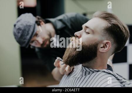 Seitenansicht des bärtigen Mannes, der seinen Bart vom Friseur im Friseurladen schneiden ließ Stockfoto