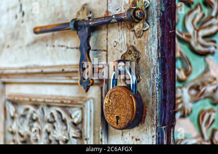 An einer Klammer an einer teilweise geöffneten Tür ist ein Messing-Vorhängeschloss aufgehängt. Ein altmodischer und wetterhalsigem Messingverschluss ist ebenfalls im Bild zu sehen. Stockfoto