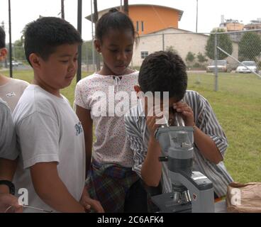 Austin Texas, USA, April 2004: Schüler der 6. Und 7. Klasse erfahren auf der von der City of Austin gesponserten Outdoor-Veranstaltung Blue Thumb mehr über Wasser- und Abwasserprobleme. Ein hispanischer Junge schwärmt durch das Mikroskop, während Klassenkameraden zuschauen. ©Bob Daemmrich Stockfoto