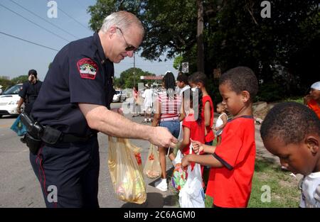 Austin Texas, USA, 19. Juni 2004: Weißer Polizist verteilt Süßigkeiten an den jungen Schwarzen auf der Juneteenth Parade Route. ©Bob Daemmrich Stockfoto