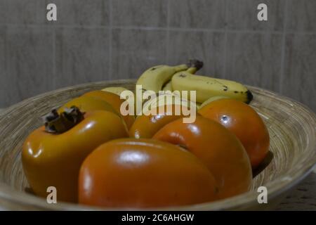 Früchte, typisch für Brasilien, Kaki und Banane in einem Holzkorb im Inneren von Brasilien, Südamerika in Zoom-Foto mit Keramikfliesen Hintergrund Stockfoto