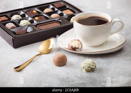 Box von Luxus Schokolade Bonbons Auswahl mit Tasse schwarzen Kaffee und goldenen Löffel auf hellem Hintergrund. Stockfoto