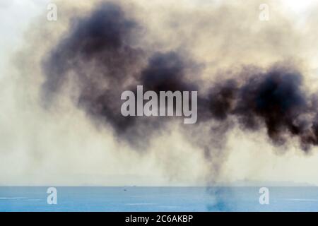 Auspuffrohr des Fährschiffs mit schwarzem dichtem Rauch, der herauskommt, und Himmel mit Wolken auf dem Hintergrund. Luftverschmutzung. Stockfoto