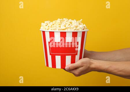 Männliche Hände halten Eimer mit Popcorn auf gelbem Hintergrund Stockfoto