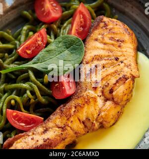 Lachssteak mit grünen Pici-Nudeln, Kirschtomaten und Käsesauce. Gesundes Gericht mit rotem Fisch im Restaurant. Quadratisches Foto Nahaufnahme. Stockfoto