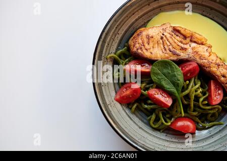 Lachssteak mit grünen Pici-Nudeln, Kirschtomaten und Käsesauce. Gesundes Gericht mit rotem Fisch im Restaurant. Weißer Hintergrund mit Kopierbereich. Stockfoto