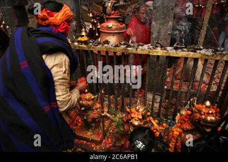 Hohepriester neben der großen Ghanta (hinduistische rituelle Glocke) und rituellen Öllampen im Hauptheiligtum im Dakshinkali Tempel in der Nähe von Kathmandu, Nepal. Einer der wichtigsten Hindu-Tempel in Nepal, der der Göttin Kali gewidmet ist, ist für seine Tieropfer bekannt, die im Hauptheiligtum stattfinden. Stockfoto